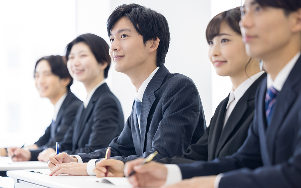 Light UPのスライダー画像。セミナーを受けるスーツを着た若い男女の社員。